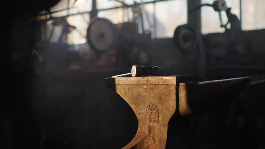 Anvil is softly lit in a workshop with blurred tools in the background