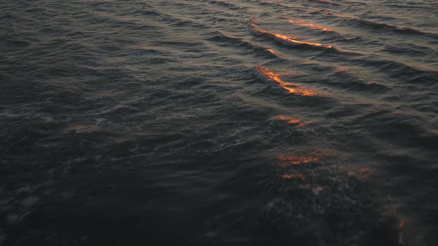 An aerial view captures the vast open ocean at sunset the dark waters surface reflecting the warm fading sunlight in patches