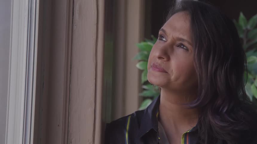 Woman smiles slightly while leaning near a window and looking out during the daytime