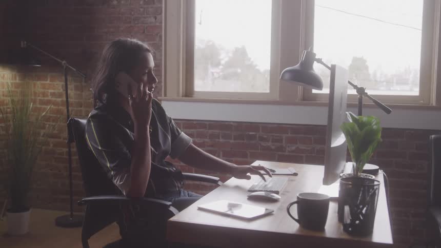 A woman types on a computer keyboard as she talks on the phone