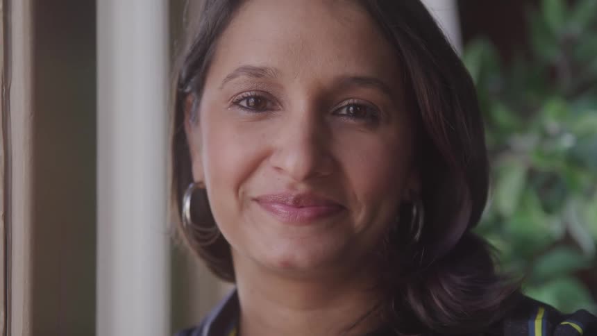 A woman smiling at the camera while standing beside a doorframe