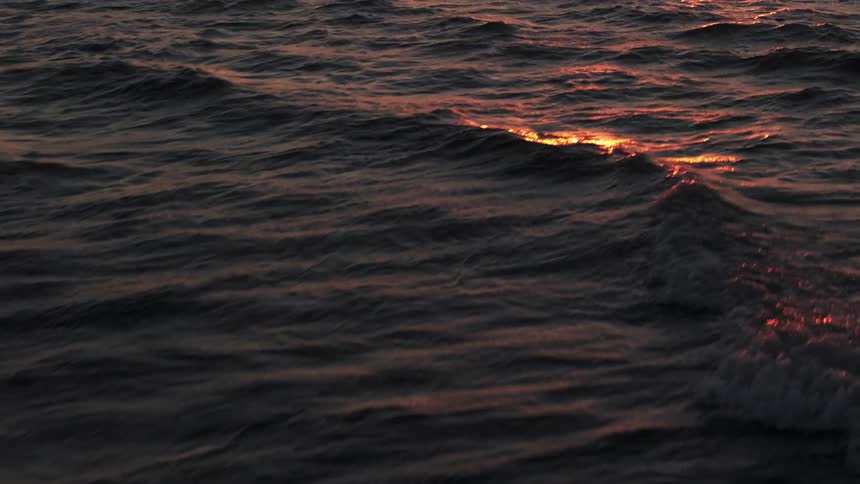 An aerial view captures the vast open ocean at sunset the dark waters surface reflecting the warm fading sunlight in patches