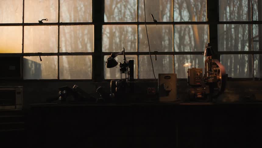 View of a workshop reveals a work table with tools illuminated by soft light coming through the windows
