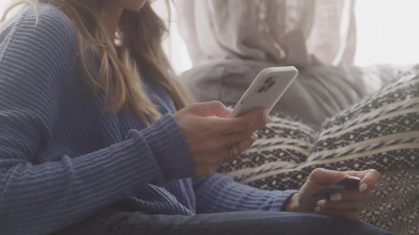A woman with long blonde hair sits on a couch holding a cell phone in her hands