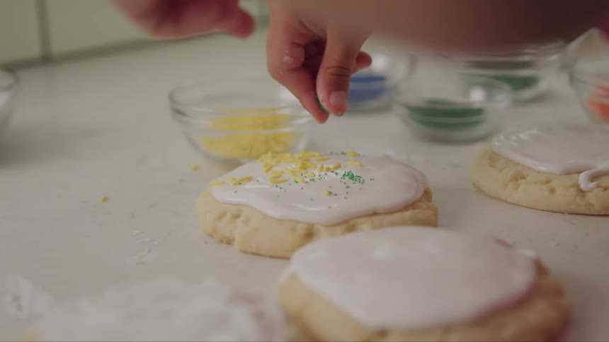 Woman adds sprinkles to a large iced cookie