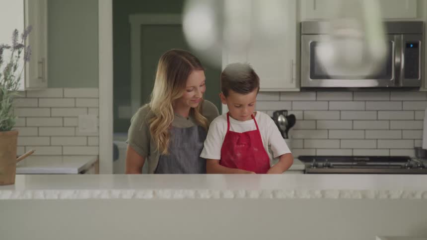 A mother and son are cooking or baking together in a bright modern kitchen