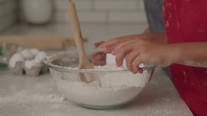 A man is cracking an egg on the rim of a glass bowl and adds it to the flour
