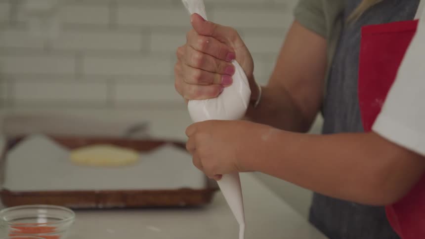 A woman and child are moving a frosting piping bag around in a kitchen