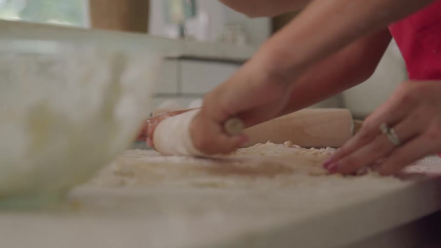 Woman dusts dough with flour while another person rolls it out during the daytime