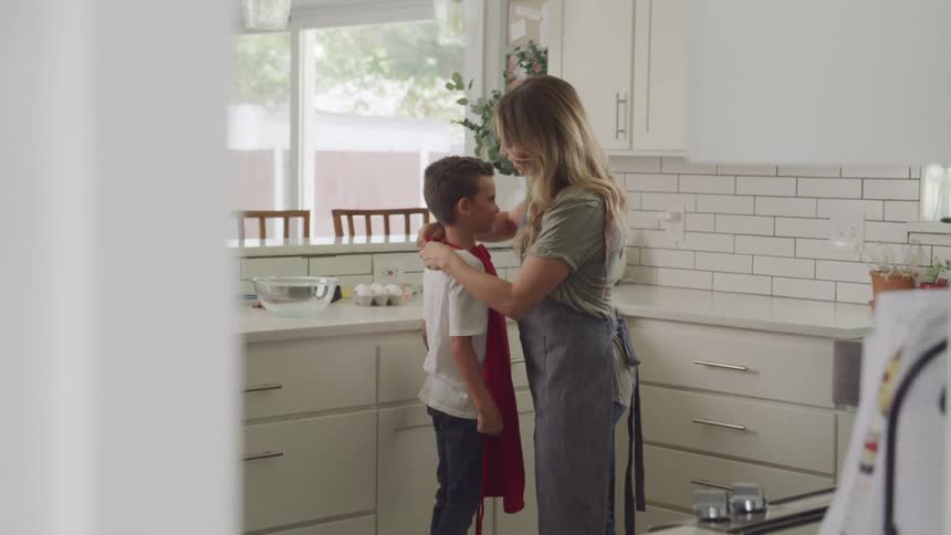 Mom tying her apron to her son in the kitchen