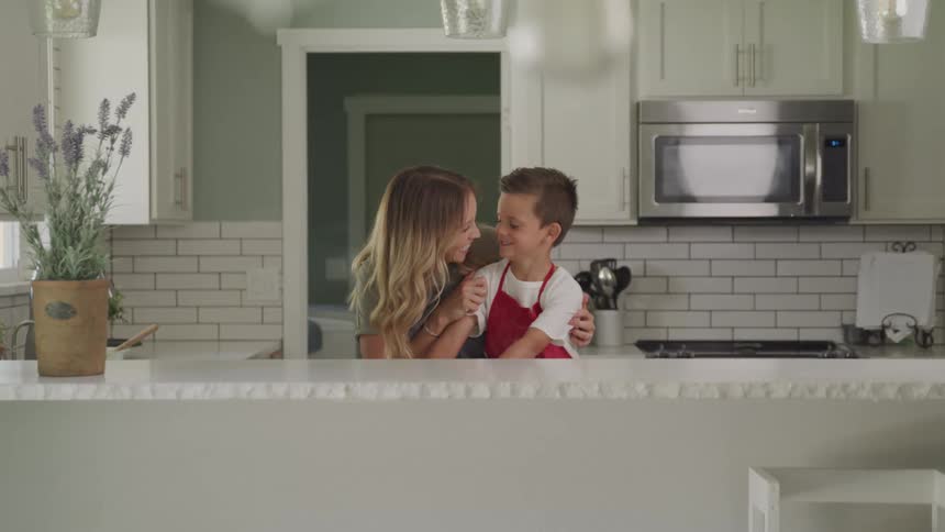 A mom hugs her son who is wearing an apron in a kitchen