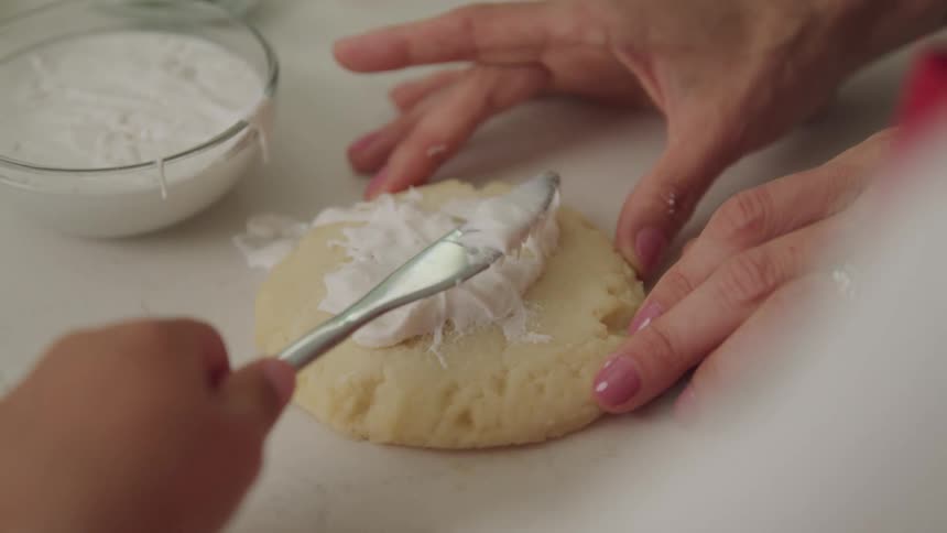 Mother holds a large pastry stationary while her child ices it