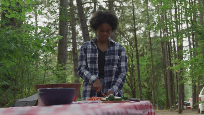 A young woman is making a salad on a camping table in the forest