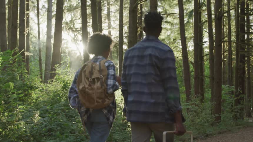 Man and woman walk along a path past the woods with a cooler on a sunny day
