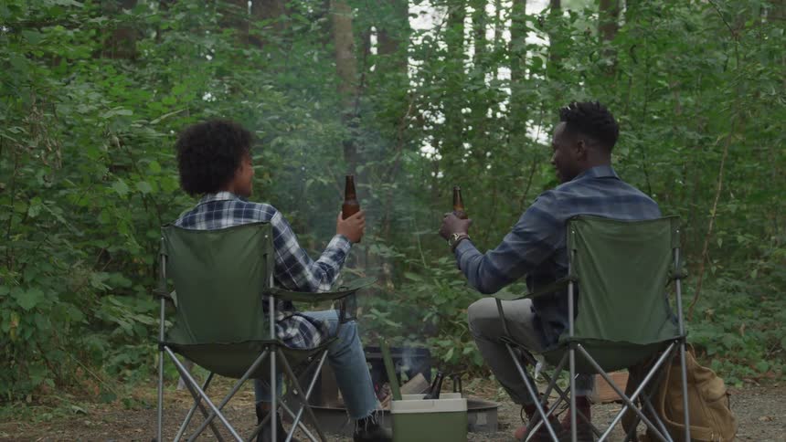 Man and woman are drinking a beer by the bonfire