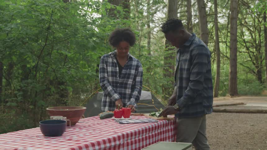 2 boys cutting ingredients on a table in the middle of a forest