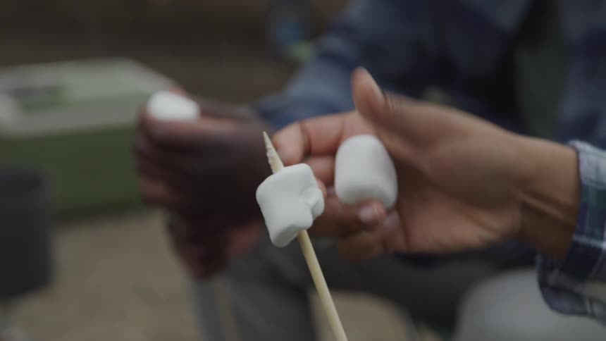Close up of two peoples hands putting marshmallows on a stick
