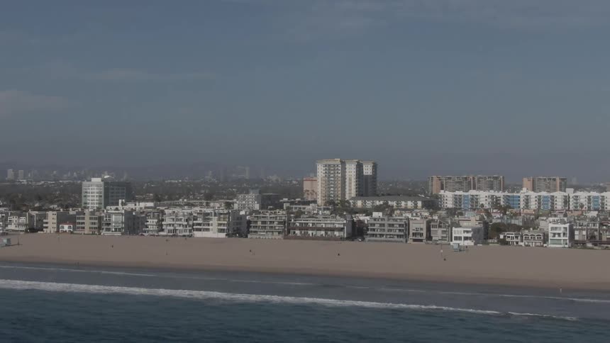 An aerial of a sandy beach lined with buildings with a city skyline visible in the distance