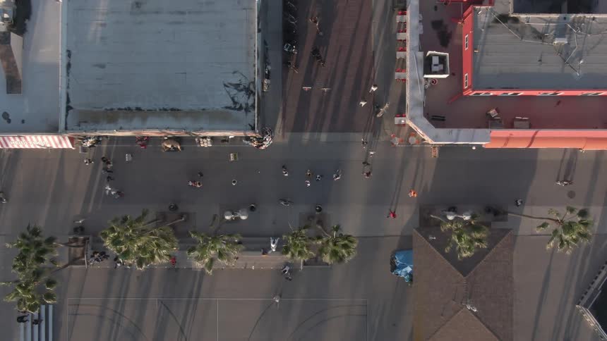 An aerial view of a city street with palm trees and people walking framed by buildings on either side