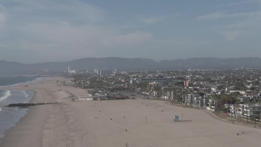 Aerial view of a long beach with the city in the background and some people walking along the sand