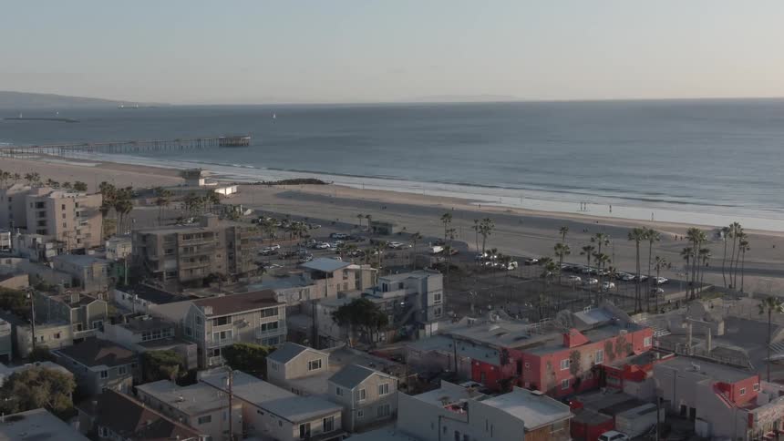 An aerial view of a densely populated urban area adjacent to a sandy beach with the ocean stretching to the horizon and a pier visible in the distance