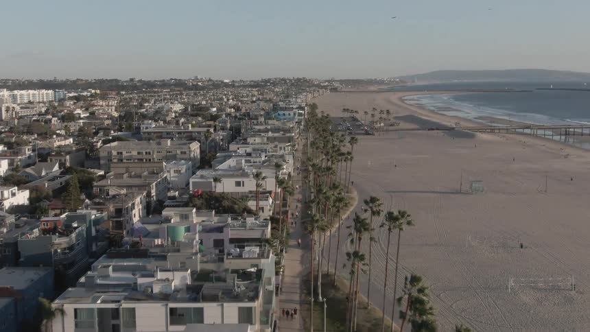 An aerial view of a long sandy beach stretching along a coastline dotted with buildings and palm trees