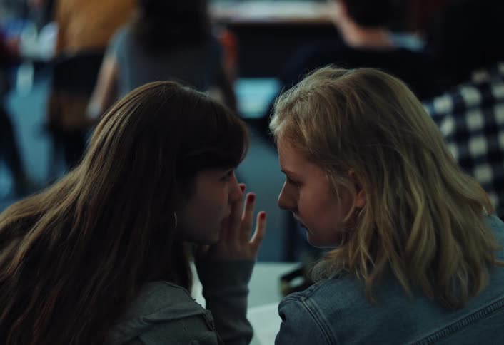 Two girls are whispering to each other in a classroom
