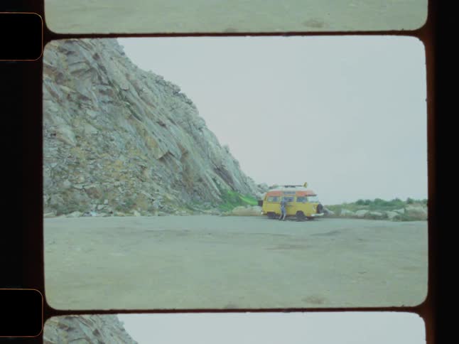 A man has parked his campervan in a flat area next to a mountain
