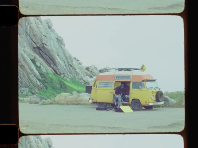Vintage footage of surfer putting on wetsuit next to vw bus at the beach