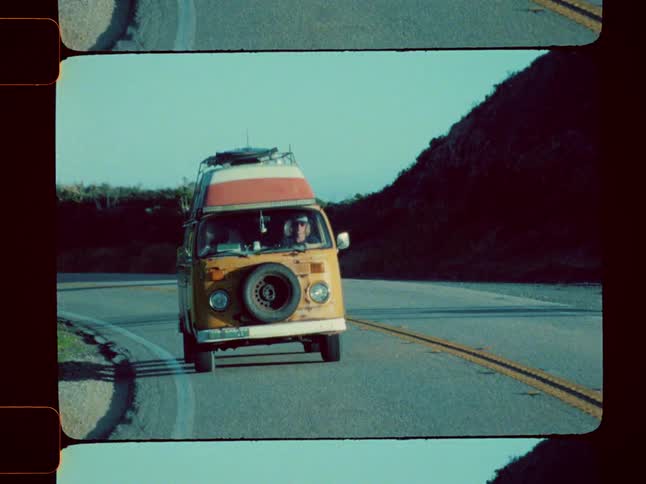 Blonde man drives a colorful van along a highway through hilly terrain under a blue sky
