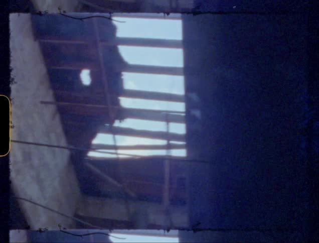 A closeup view of the exposed roof framework of a crumbling building set against a bright blue sky with sunlight streaming through