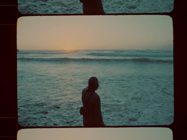 Man silhouetted against the surf stands on the shore as the sun rises