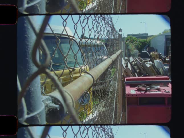 A yellow van is partially visible through a chainlink fence in an outdoor storage area