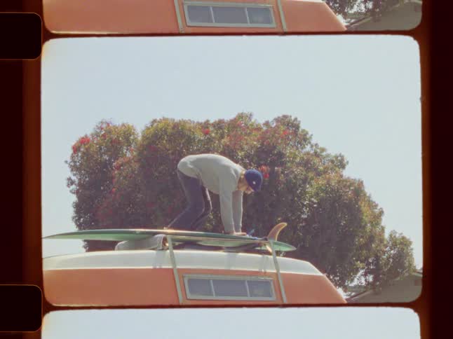 A man is on top of a campervan securing a surfboard