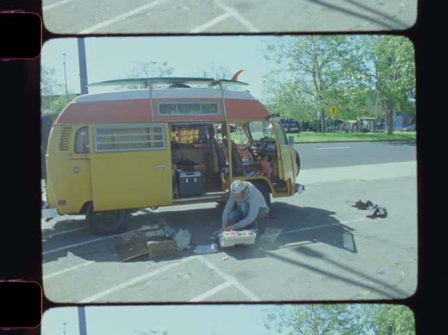 Male crouching down in front of vw bus in parking lot packing up supplies in tool kit