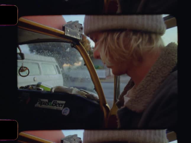 A young man with a beanie and long blonde hair stands at the open door of a van organizing luggage for a morning journey