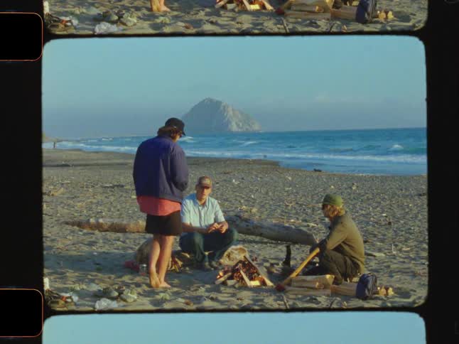 3 people talking around a fire in the middle of the beach