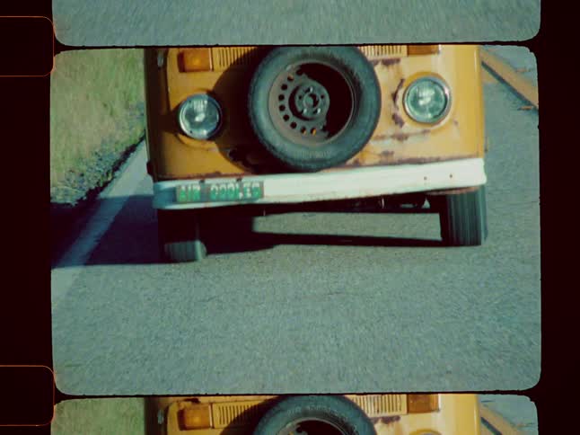 A vintage yellow volkswagen van is captured in motion driving down a road presented within a distinct analog film frame