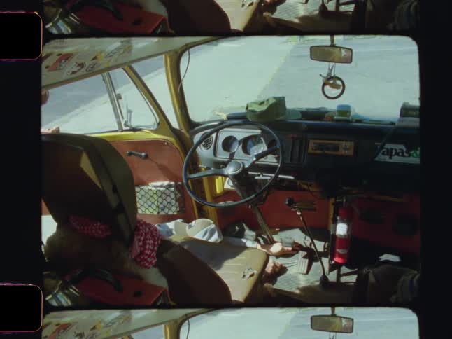 Van with an open door and a man crouching outside reaching under the accelerator pedal with a screwdriver on a sunny day