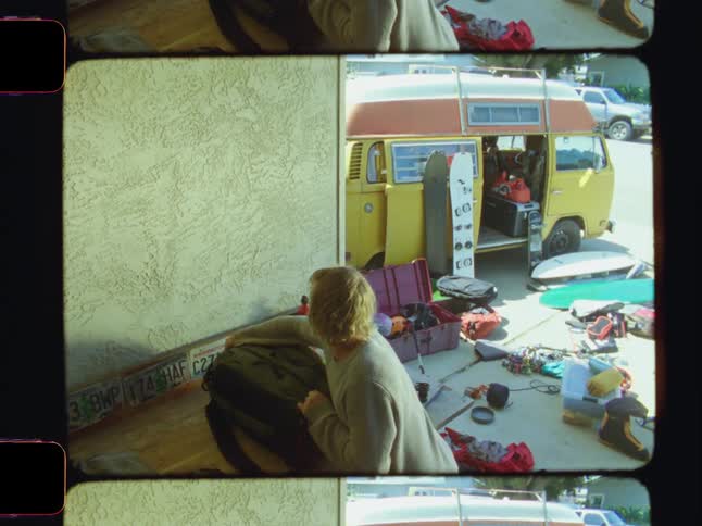 A man organizes bags and scattered items near a parked yellow van on a sunny day preparing for a trip