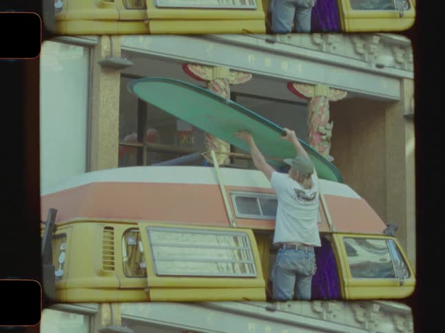 Guy putting a surfboard on top of a van