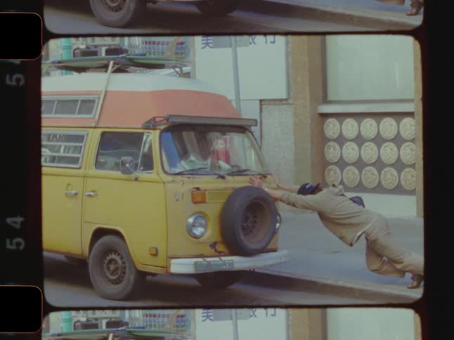 A man pushes an old van down a city street