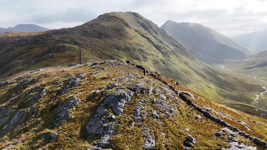 An adult hiker is standing on a mountaintop overlooking a valley