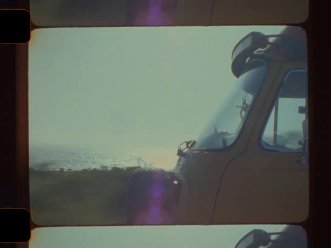 A yellow van with a red and white poptop roof is seen in motion with blurred trees visible through the side window