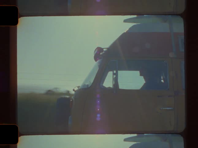 A young man with blonde hair and sunglasses drives a yellow van along the oceans edge