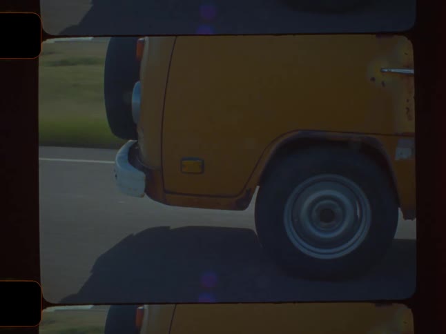 A yellow van including a wheel bumper and part of the body moving along an asphalt road