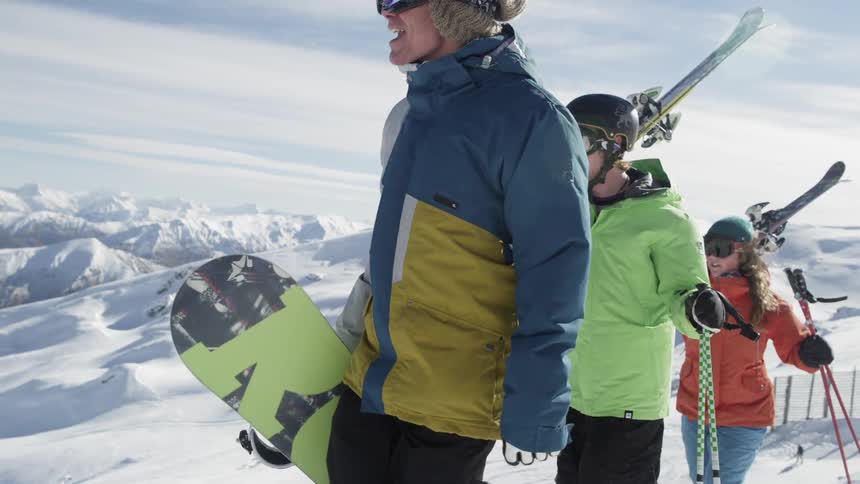 Three kids walking on top of a hill preparing to snowboard