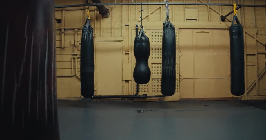 Several black punching bags hang from a metal beam on the ceiling of a gym