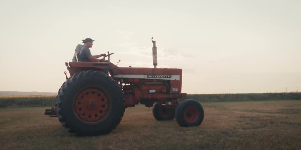 Two men ride on a tractor through a grass covered field