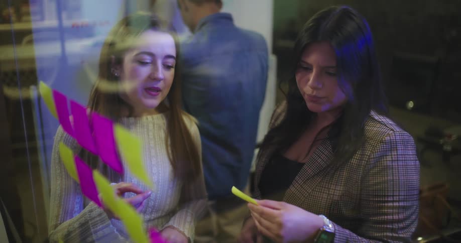 Two women talk and look at post it notes on the glass